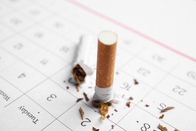 Photo of Broken cigarette on calendar sheet, closeup. Quitting smoking concept
