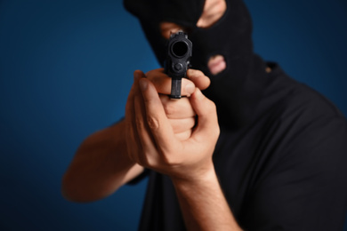 Photo of Man in mask holding gun against dark blue background, focus on hands
