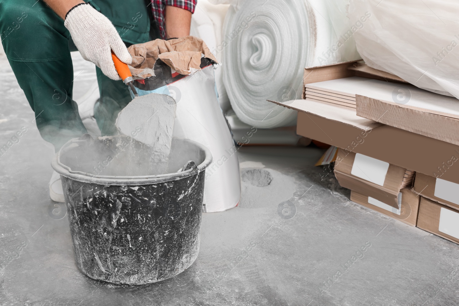 Photo of Worker with cement powder and trowel mixing concrete in bucket indoors, closeup