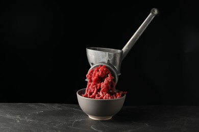 Metal meat grinder with beef mince on dark textured table against black background