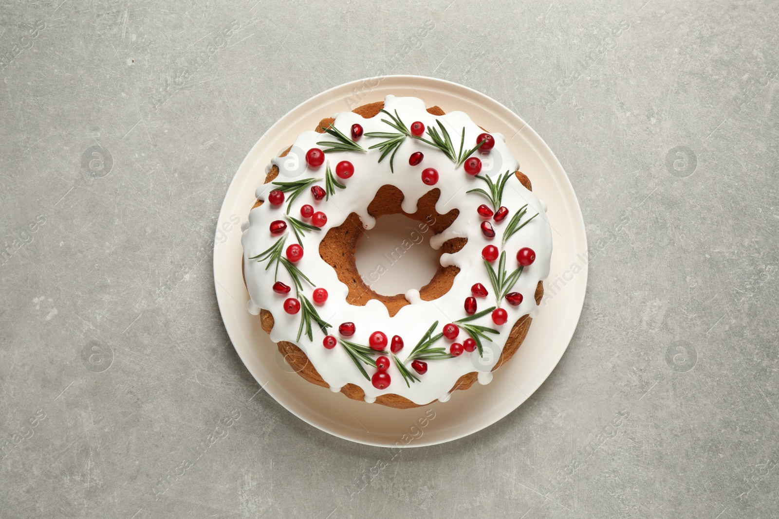 Photo of Traditional Christmas cake decorated with glaze, pomegranate seeds, cranberries and rosemary on light grey table, top view