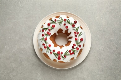 Photo of Traditional Christmas cake decorated with glaze, pomegranate seeds, cranberries and rosemary on light grey table, top view