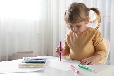 Photo of Cute little girl drawing with marker at white table indoors. Child`s art