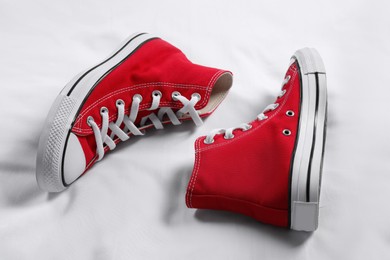 Pair of new stylish red sneakers on white fabric