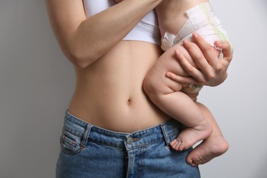 Photo of Mother with bare belly holding her baby on light grey background, closeup