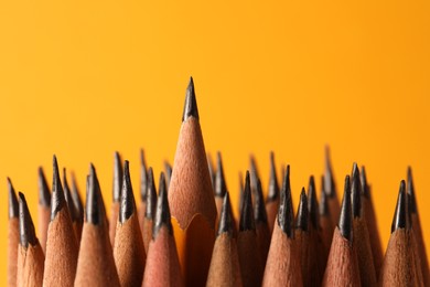 Many sharp graphite pencils on orange background, closeup. Space for text