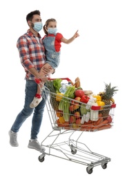 Photo of Father and daughter in medical masks with shopping cart full of groceries on white background