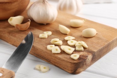 Aromatic cut garlic, cloves, bulbs and knife on white wooden table, closeup