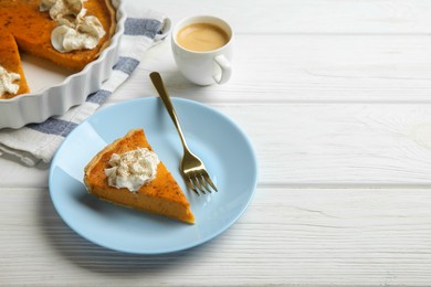 Photo of Delicious pumpkin pie with whipped cream, fork and cup of coffee on white wooden table. Space for text