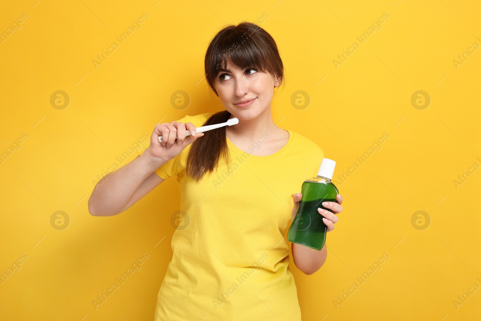 Photo of Young woman with mouthwash and toothbrush on yellow background