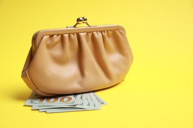 Stylish beige leather purse with dollar banknotes on yellow background. Space for text