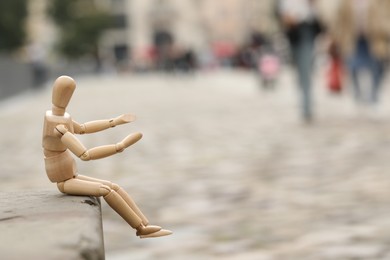 Wooden human figure sitting on curb outdoors, space for text