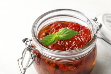 Jar with sun dried tomatoes on light table, closeup