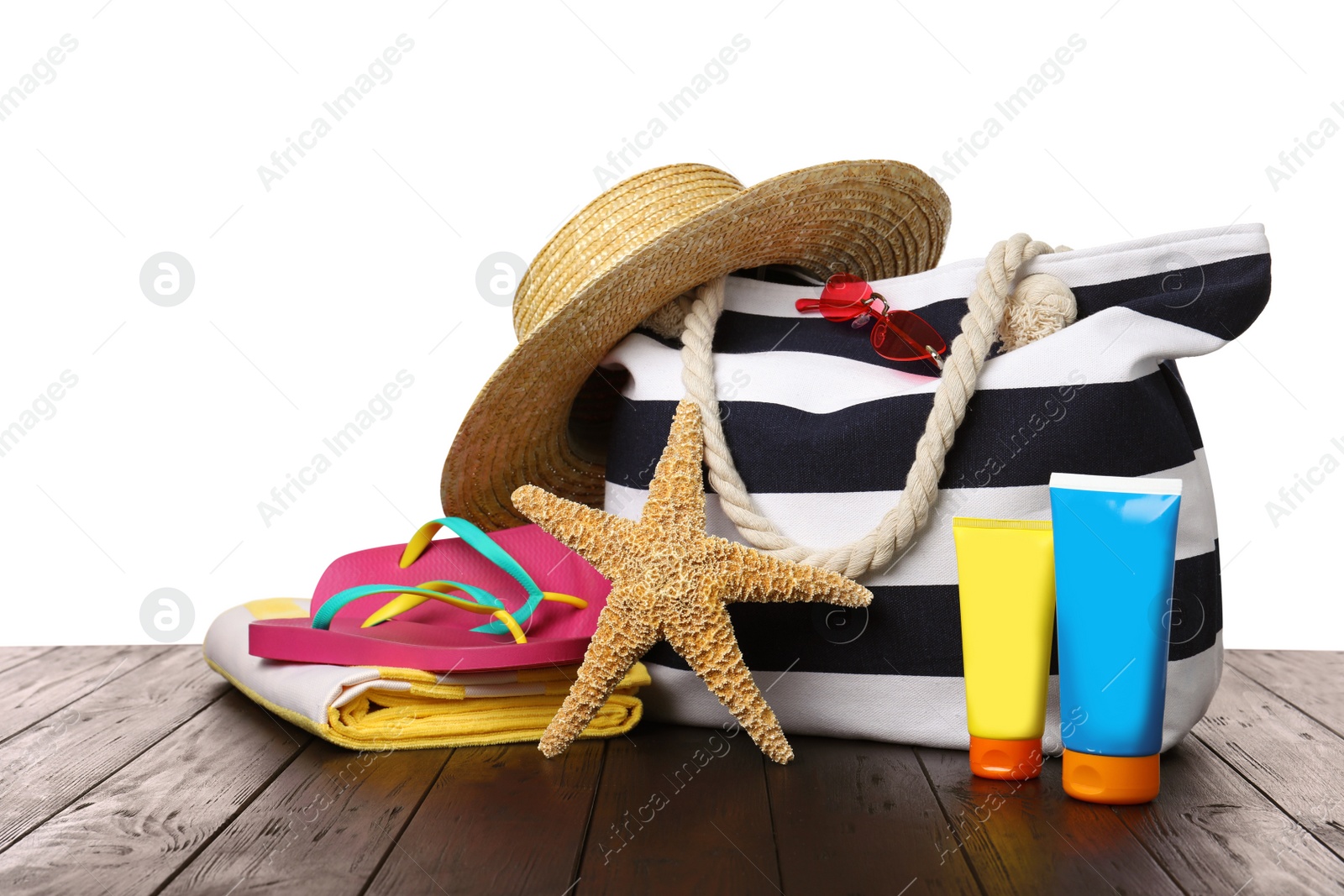 Photo of Stylish bag with beach accessories on wooden table against white background