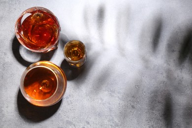 Photo of Different delicious liqueurs in glasses on grey table, flat lay. Space for text