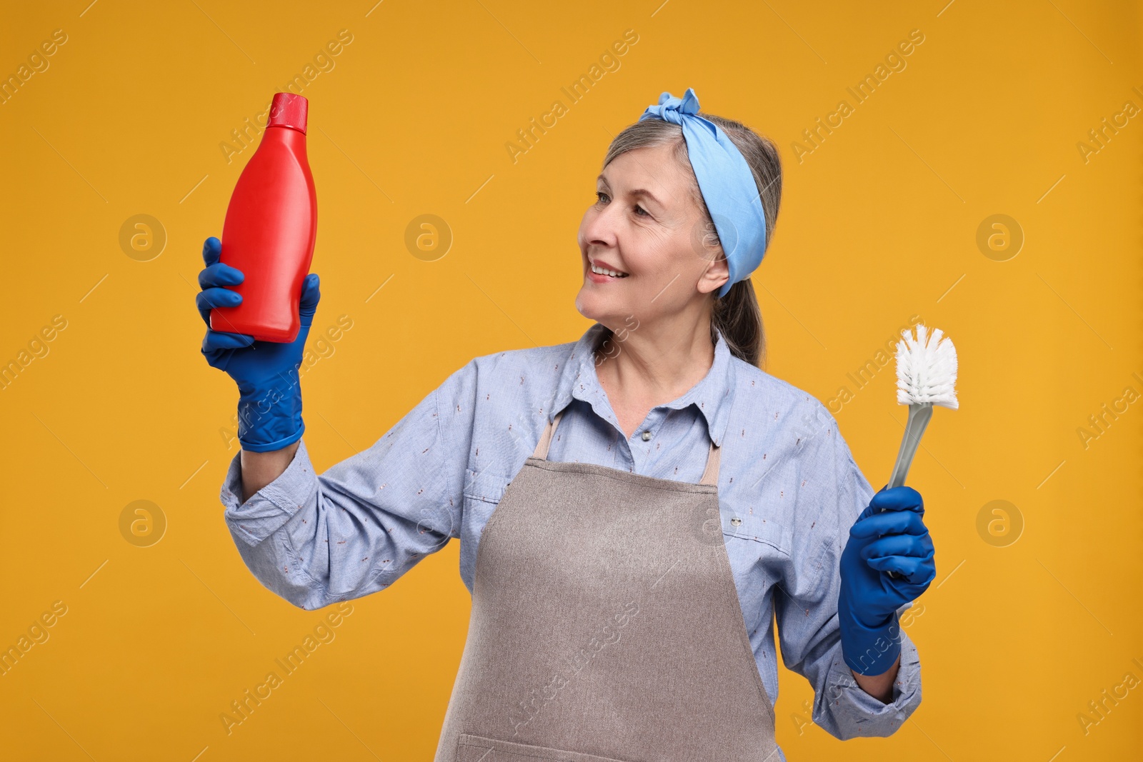 Photo of Happy housewife bottle of detergent and brush on orange background