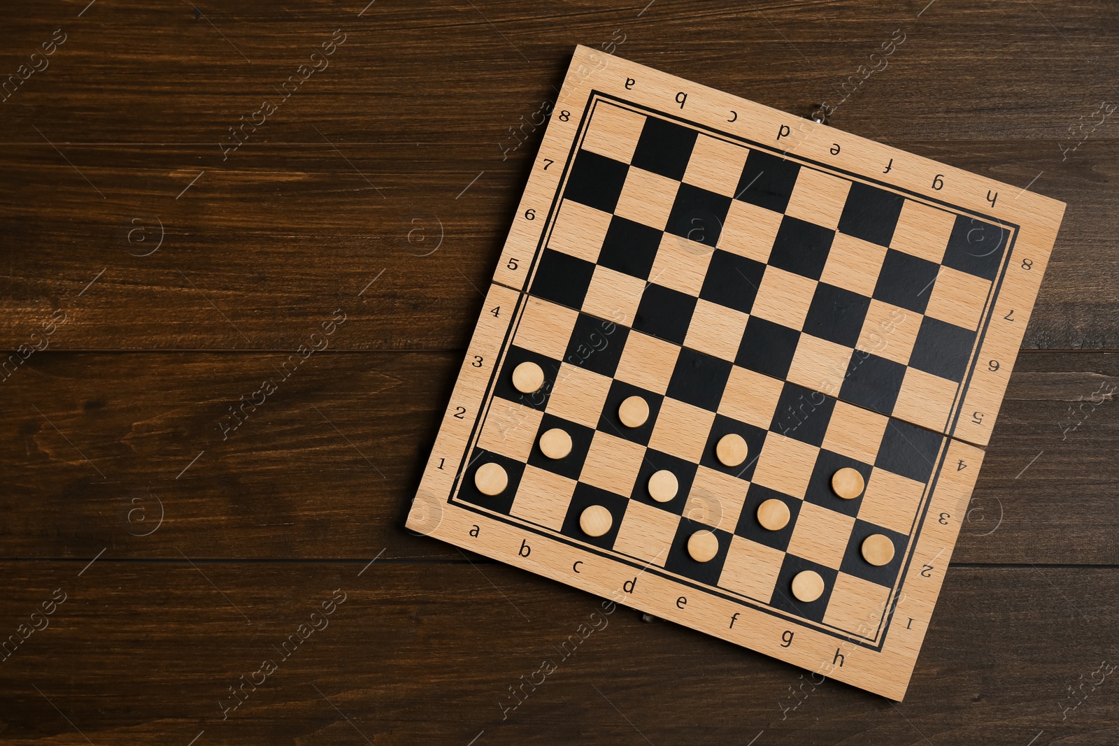 Photo of Checkerboard with game pieces on wooden table, top view. Space for text