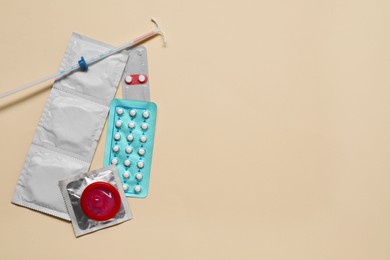 Photo of Contraception choice. Pills, condoms and intrauterine device on beige background, flat lay. Space for text