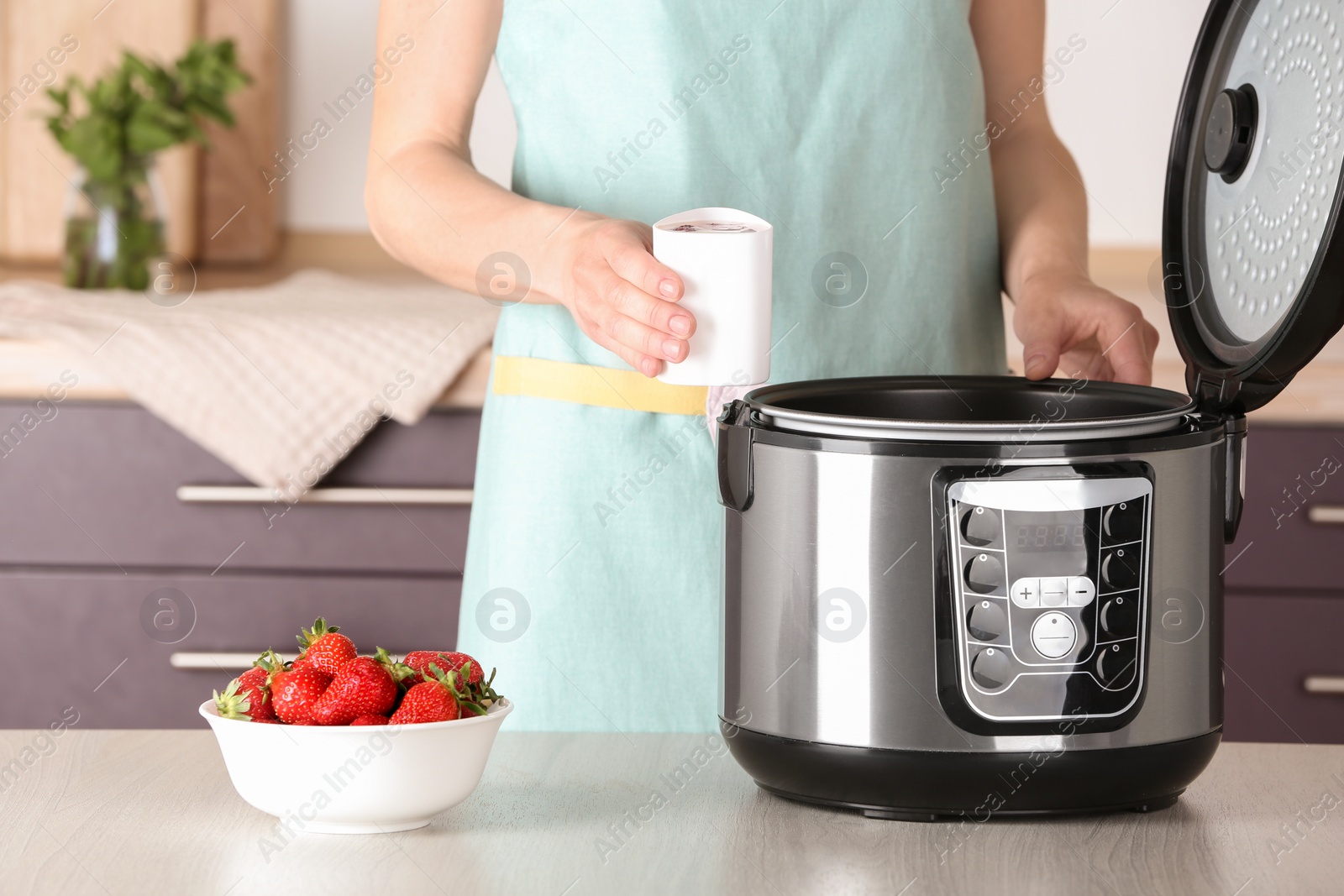 Photo of Woman holding container with delicious fresh yogurt made in modern multi cooker at table, closeup