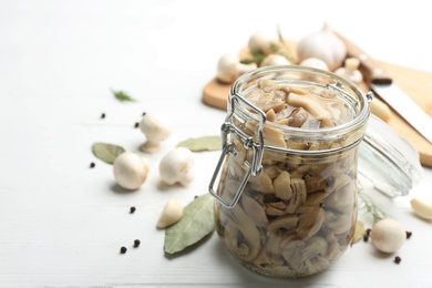 Photo of Glass jar of pickled mushrooms on white wooden table. Space for text