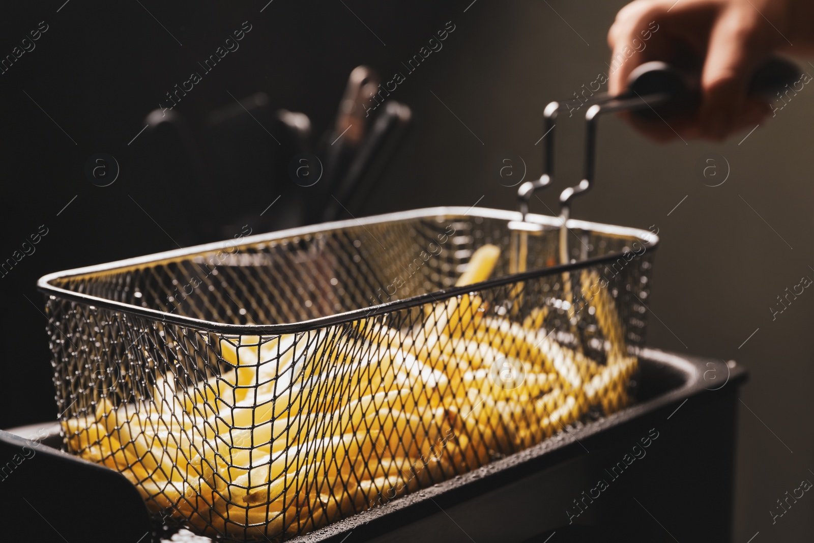 Photo of Chef cooking delicious french fries in hot oil, closeup