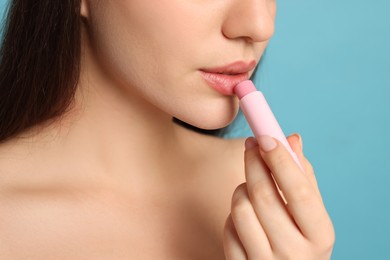 Photo of Young woman applying lip balm on turquoise background, closeup