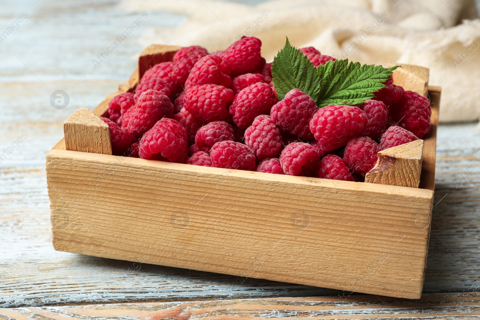 Photo of Crate of delicious fresh ripe raspberries with leaves on wooden table