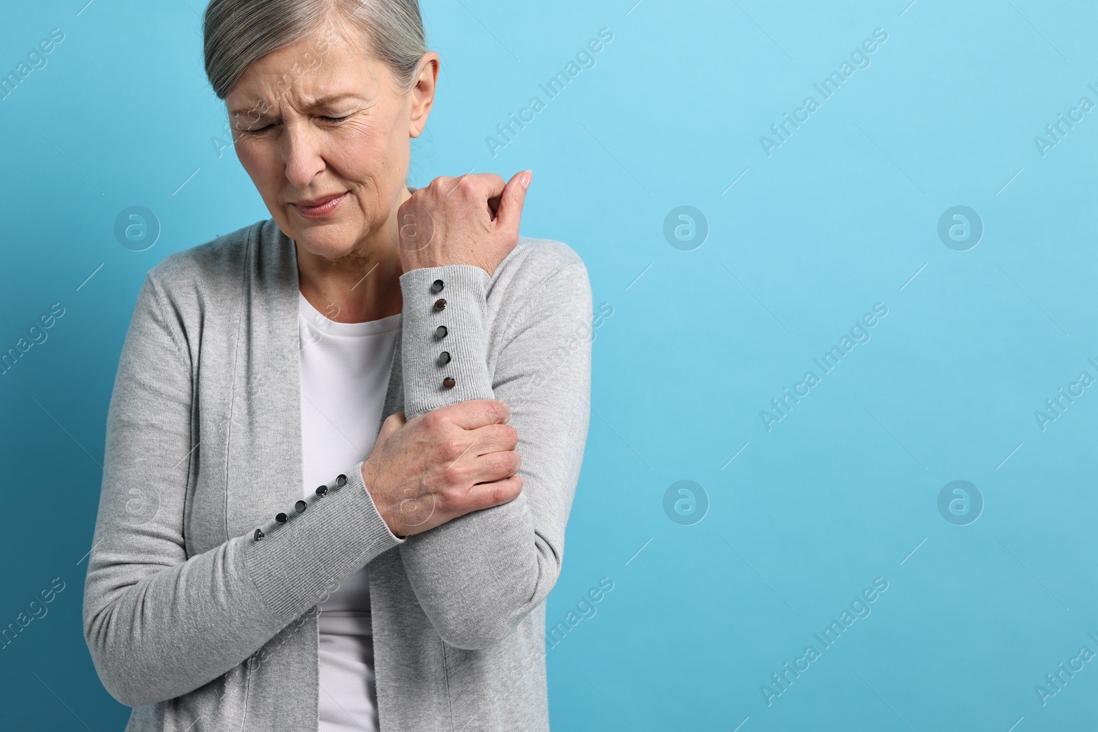 Photo of Arthritis symptoms. Woman suffering from pain in arm on light blue background