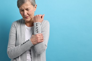 Arthritis symptoms. Woman suffering from pain in arm on light blue background