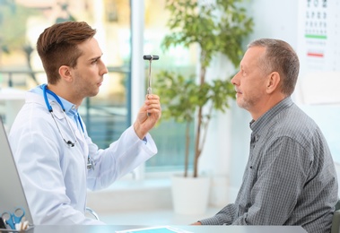 Photo of Doctor checking reflexes of mature patient in hospital
