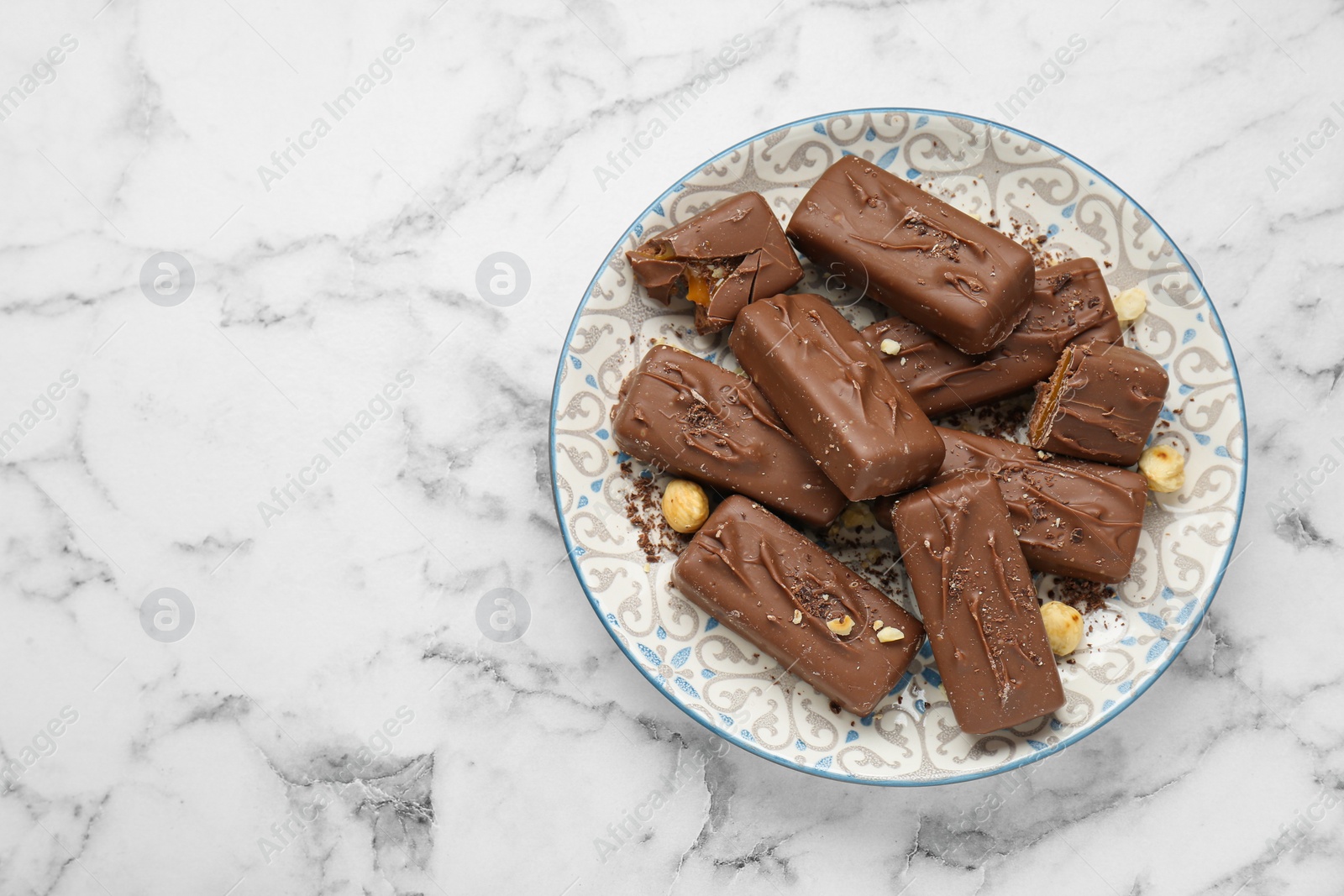 Photo of Delicious chocolate candy bars with nuts on white marble table, top view. Space for text