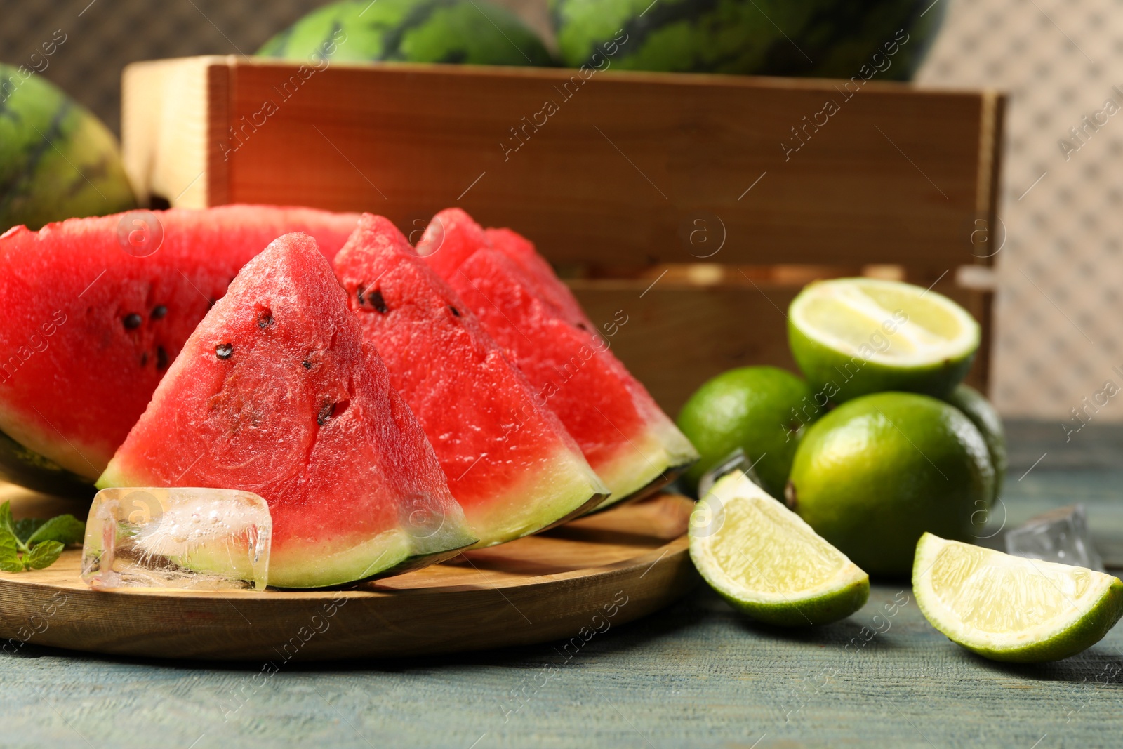 Photo of Slices of delicious watermelon, limes, ice and mint on light blue wooden table
