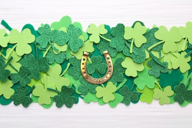 Photo of St. Patrick's day. Golden horseshoe and green decorative clover leaves on white wooden table, flat lay