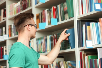 Photo of Young man taking book from shelving unit in library