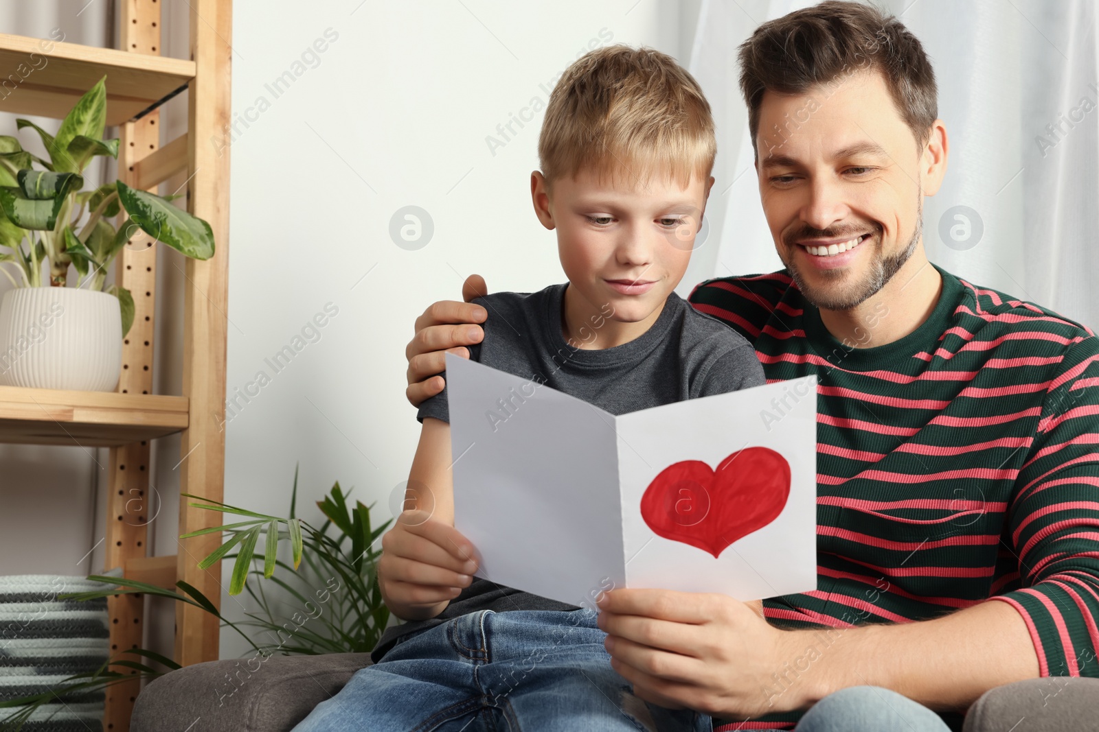 Photo of Happy man receiving greeting card from his son at home