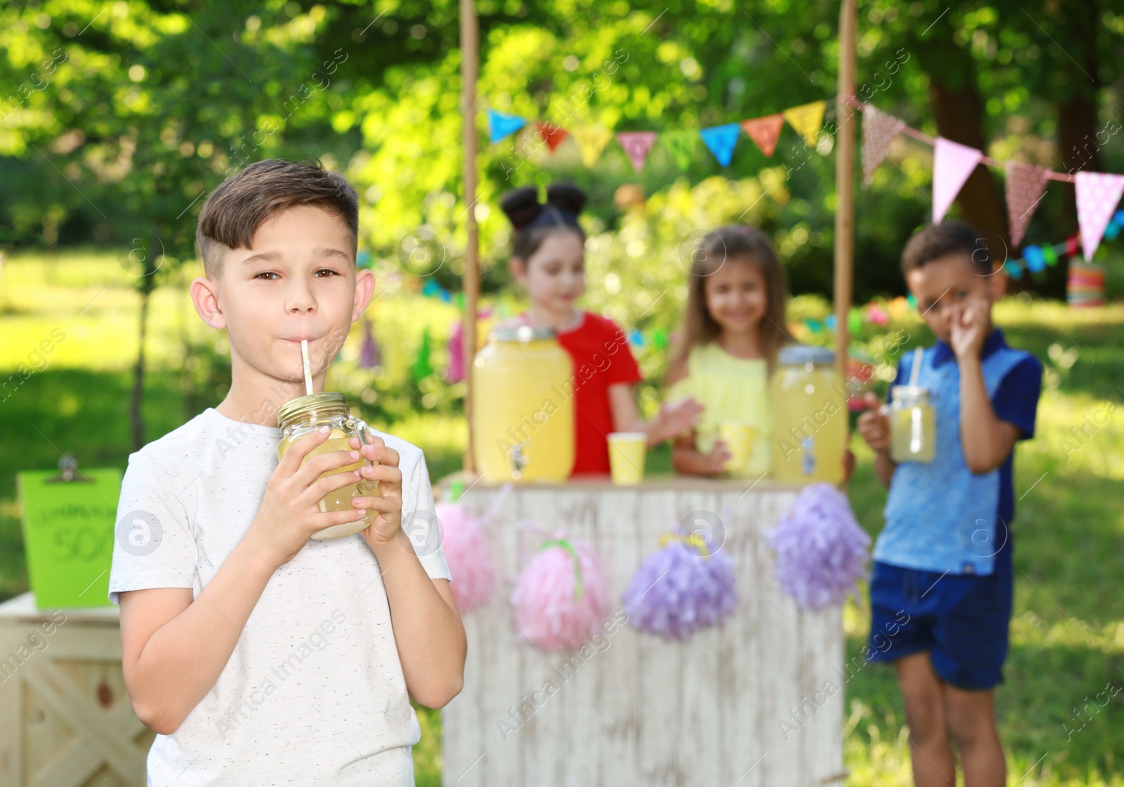 Photo of Cute little boy drinking natural lemonade in park, space for text. Summer refreshing beverage