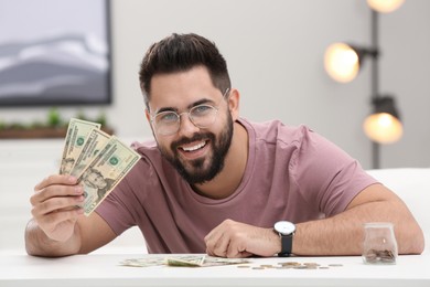 Happy young man with money at white table indoors