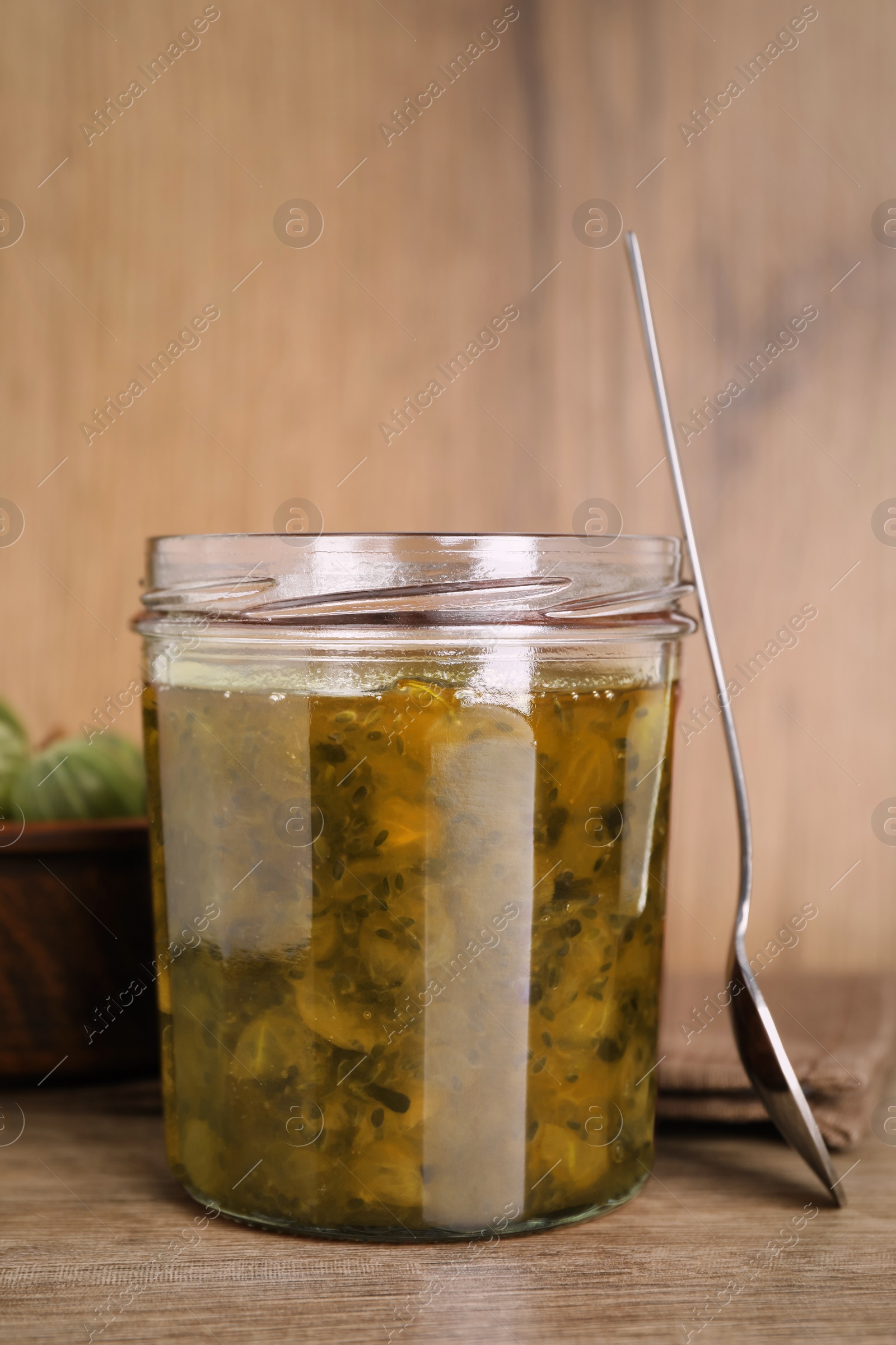 Photo of Jar of delicious gooseberry jam and bowl with fresh berries on wooden table