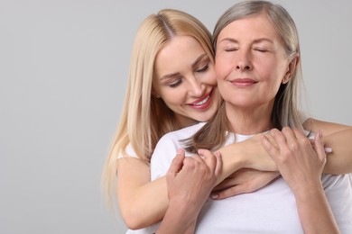 Family portrait of young woman and her mother on light grey background. Space for text