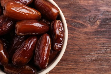 Top view of sweet dried dates in bowl on wooden background, closeup. Space for text