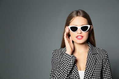 Young woman wearing stylish sunglasses on grey background. Space for text