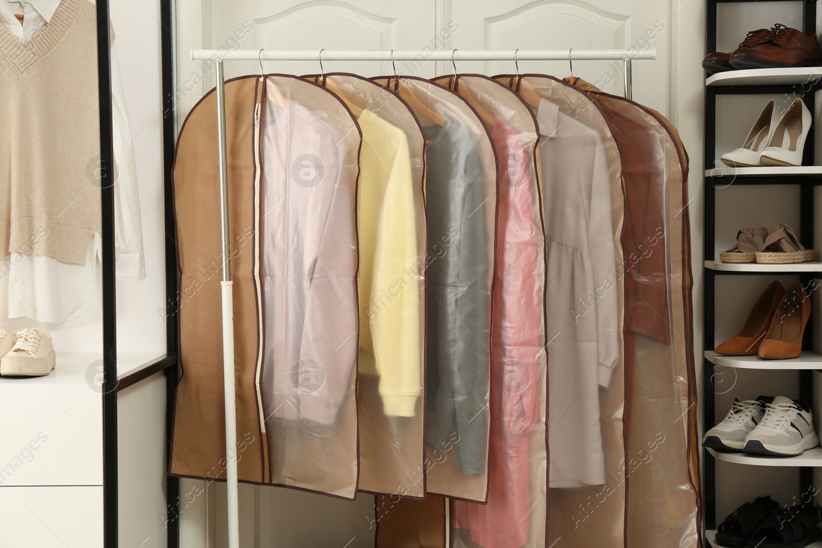 Photo of Garment bags with clothes on rack in dressing room