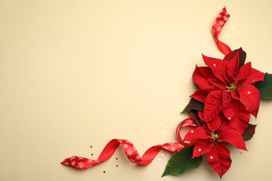 Photo of Flat lay composition with poinsettias (traditional Christmas flowers) and ribbon on beige background. Space for text