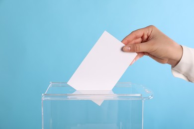 Photo of Woman putting her vote into ballot box on light blue background, closeup