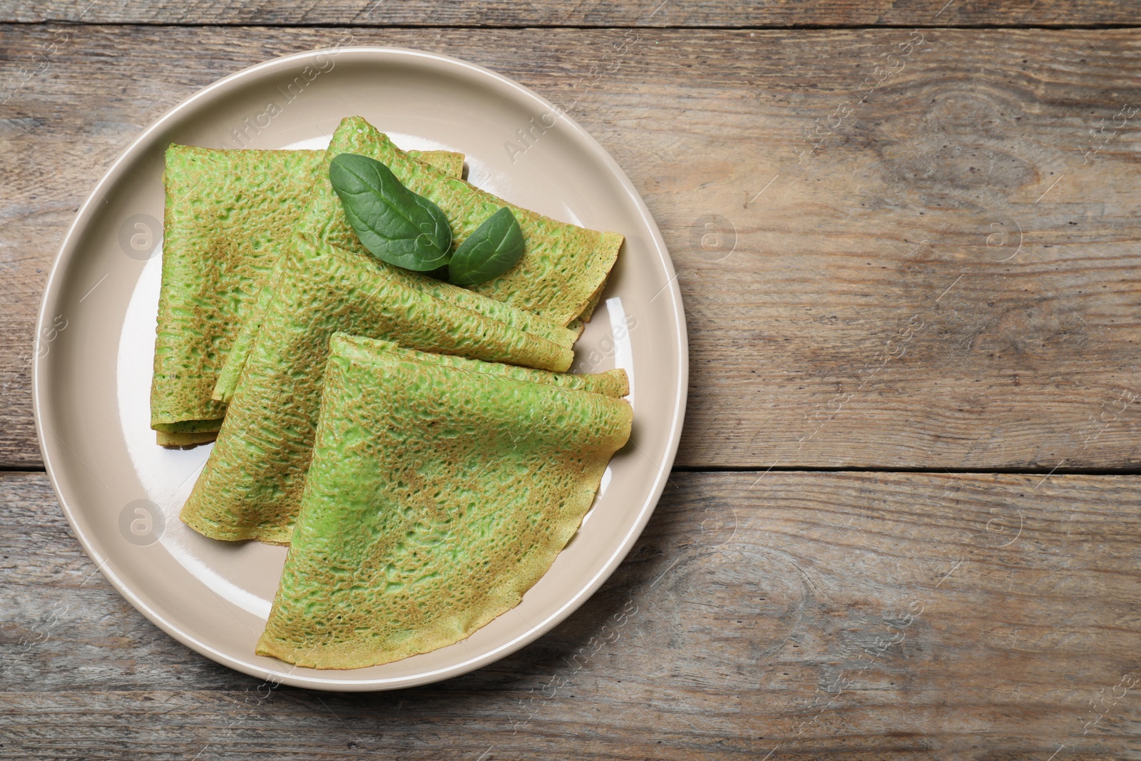 Photo of Delicious spinach crepes on wooden table, top view. Space for text