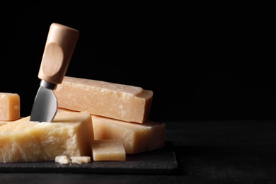 Photo of Parmesan cheese with slate plate and knife on black table, closeup. Space for text