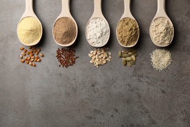 Spoons with different types of flour and ingredients on grey background, top view. Space for text