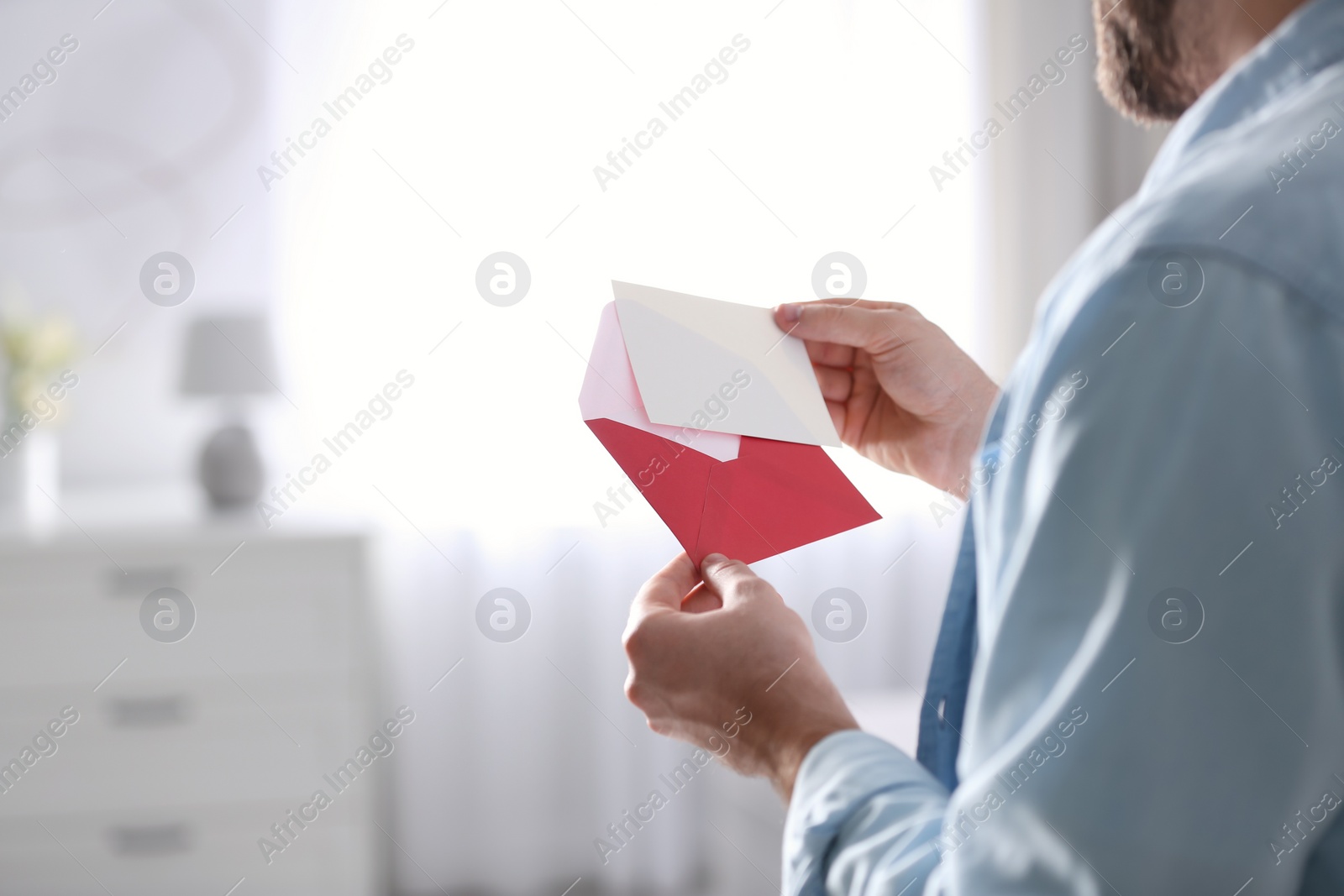 Photo of Man holding envelope with greeting card at home, closeup