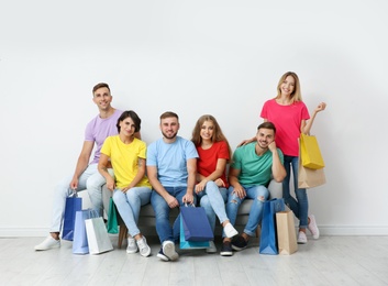 Group of young people with shopping bags sitting on sofa near light wall