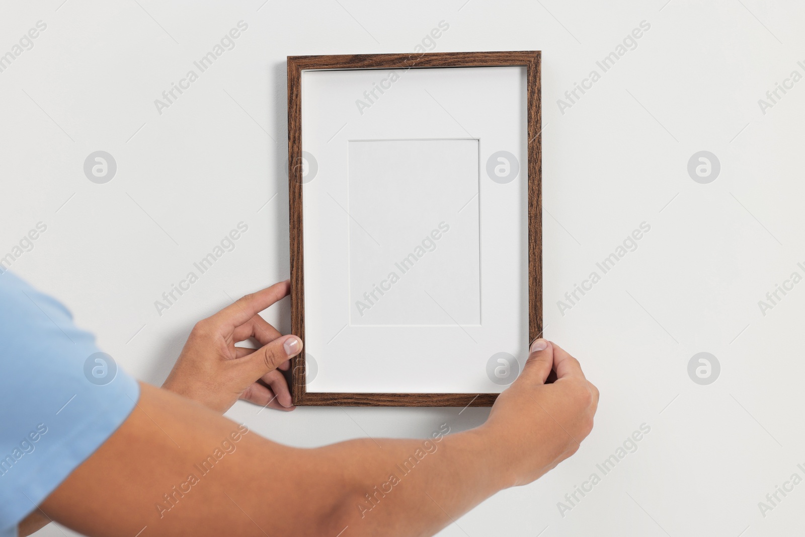 Photo of Young man hanging picture frame on white wall indoors, closeup